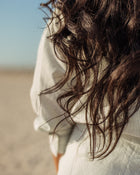 Close-up of a person with wavy hair blowing in the wind, wearing a light-coloured top.