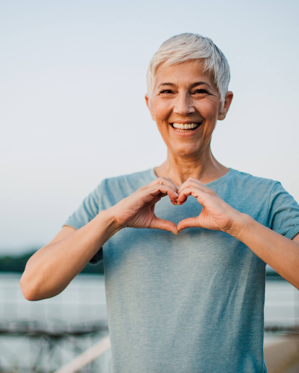 Woman making a heart shape with her hands outdoors.