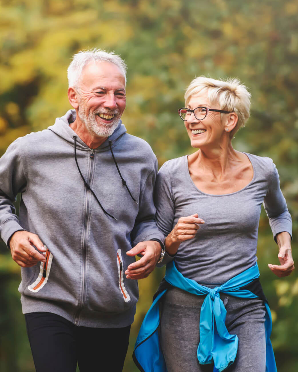 Two elderly people jogging outdoors with a blurred green background.