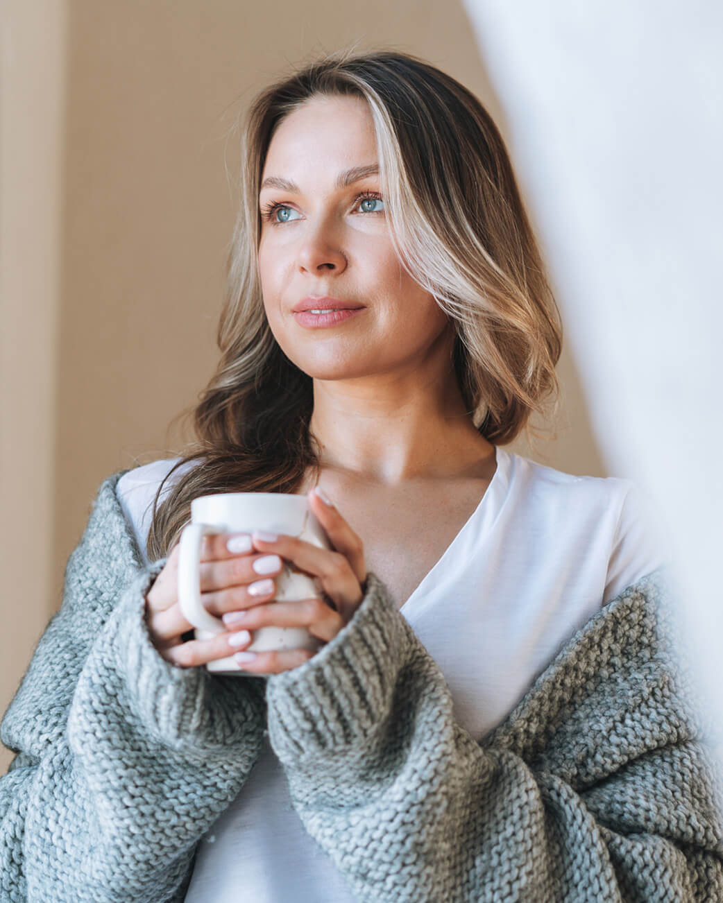 Woman holding a mug with a soft, neutral background.