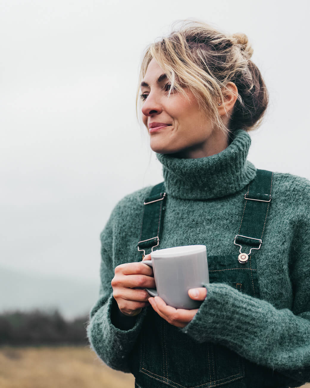 Woman holding a mug outdoors with a neutral background.