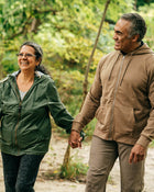 Two people walking hand in hand through a forested area.