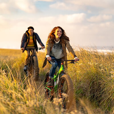 Two people riding bicycles through a grassy field with a scenic background.