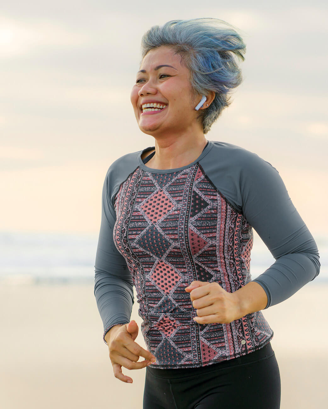 Person running on a beach with a patterned shirt and blue hair.