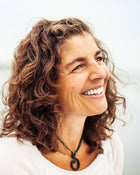 Woman with curly hair smiling against a light background.
