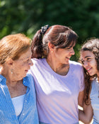 Three women standing together outdoors with a blurred green background.
