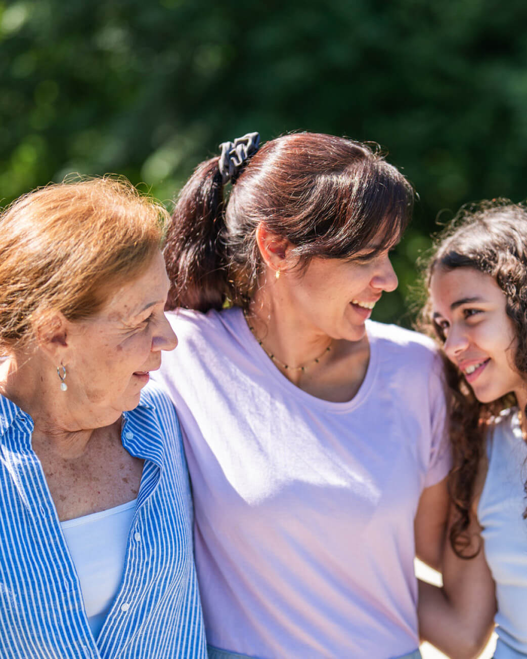 Three women standing together outdoors with a blurred green background.