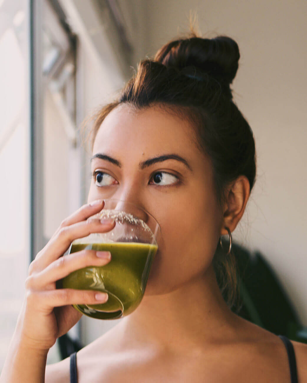 Woman drinking a green smoothie in a casual setting.