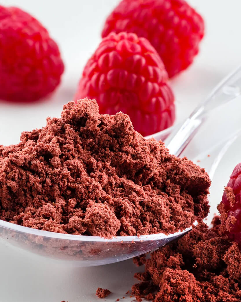 Cocoa powder in a spoon with raspberries on a white background