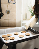 Person holding a baking tray with cookies in a kitchen setting