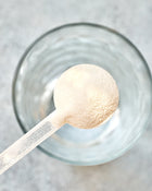 Spoonful of protein powder over a glass bowl on a light background