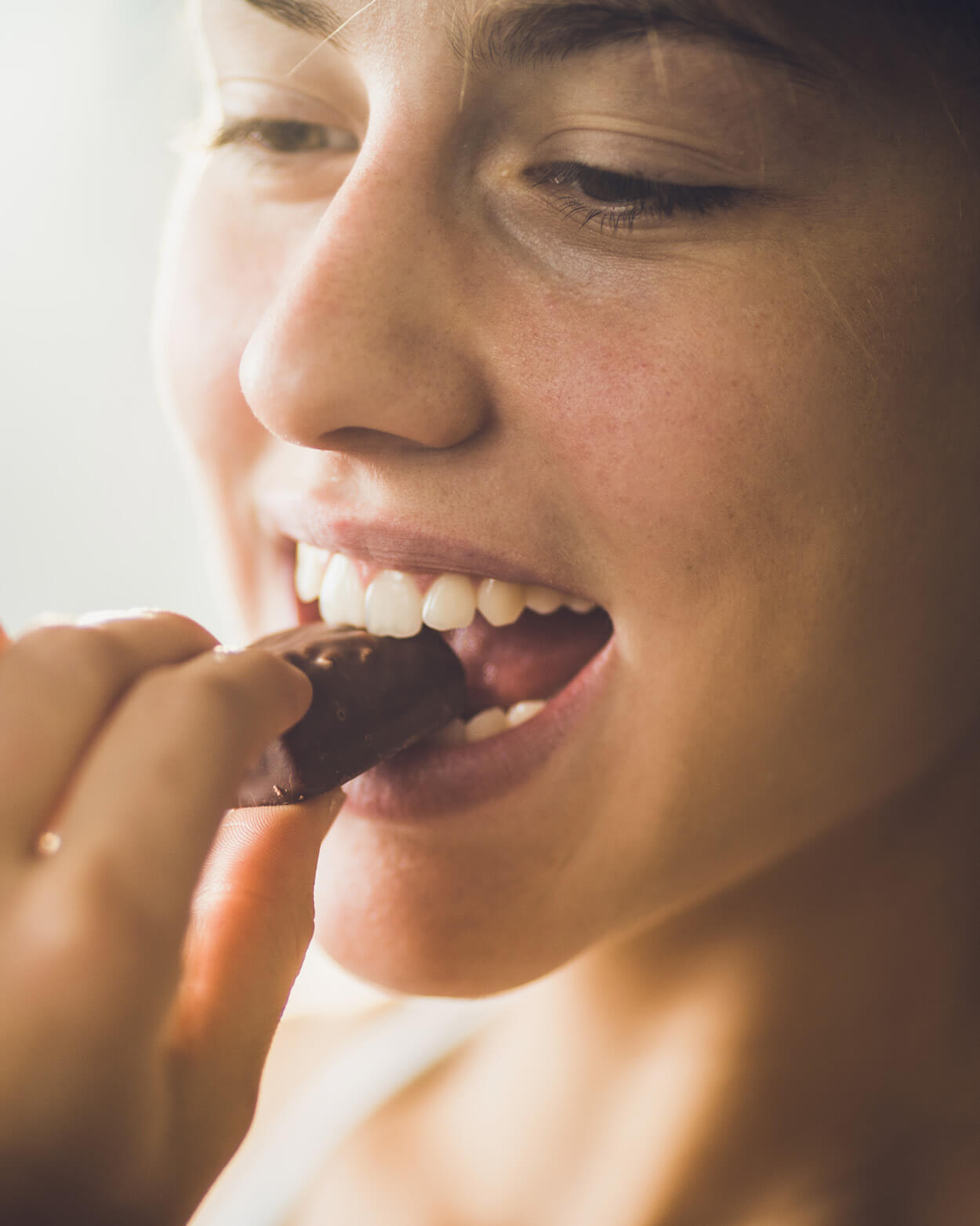 Close-up of a woman eating a chocolate bar.