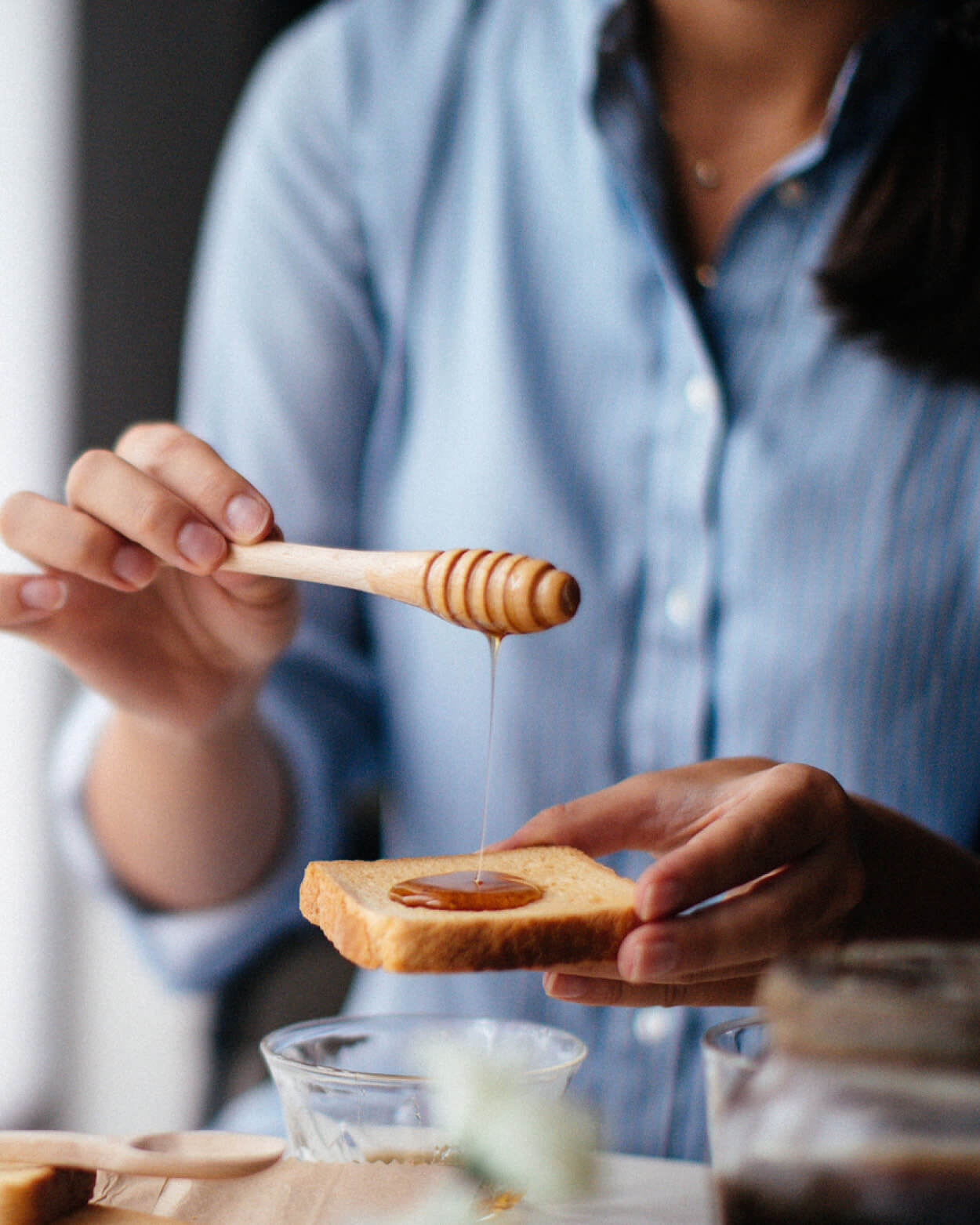 Person drizzling honey onto toast using a wooden honey dipper.