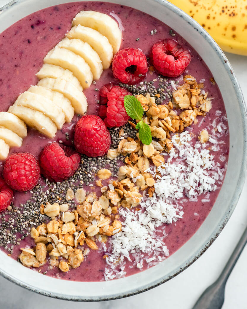 Berry smoothie bowl with banana, raspberries, granola, and coconut in a grey bowl.