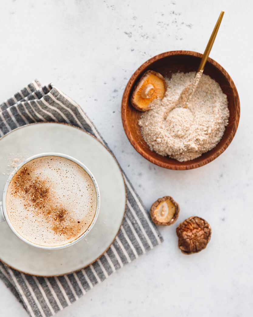 Cappuccino in a white cup with a wooden bowl of brown sugar on a light surface with mushrooms.