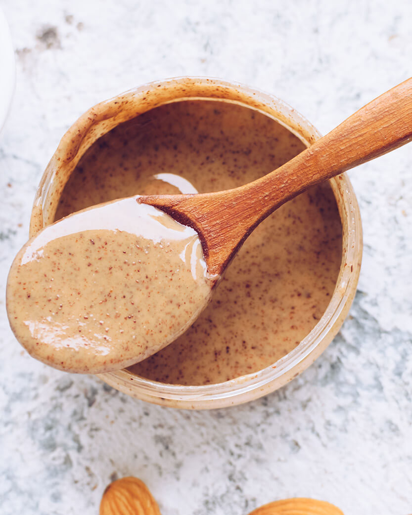 Jar of almond butter with a wooden spoon on a marble surface