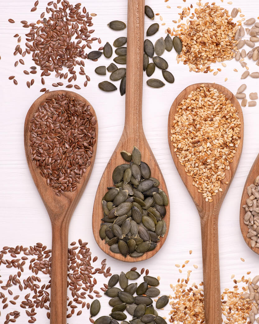 Wooden spoons filled with various seeds on a white background