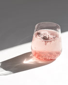 pink collagen protein powder dissolving into a glass of water on a white background with a shadow.