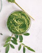 Green powder in a glass bowl with leaves on a light background