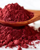 Red powder in a wooden spoon with more powder on a white background