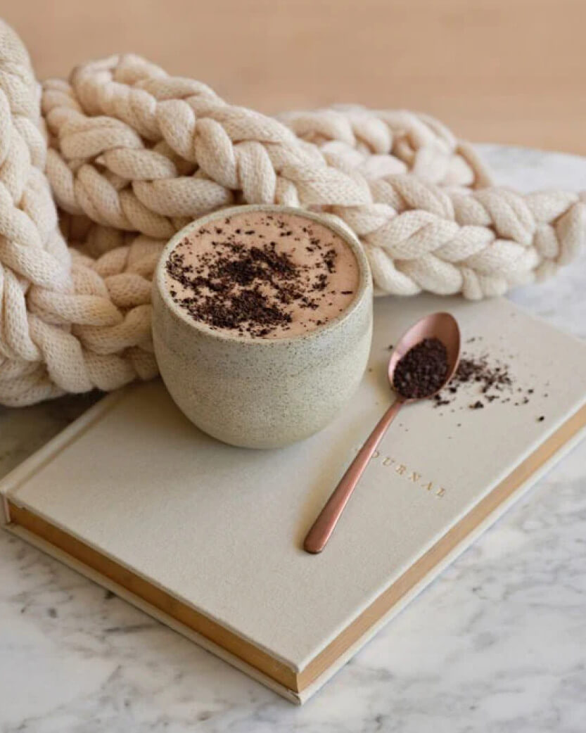 Cup of coffee with a spoon on a book, surrounded by braided yarn on a marble surface.