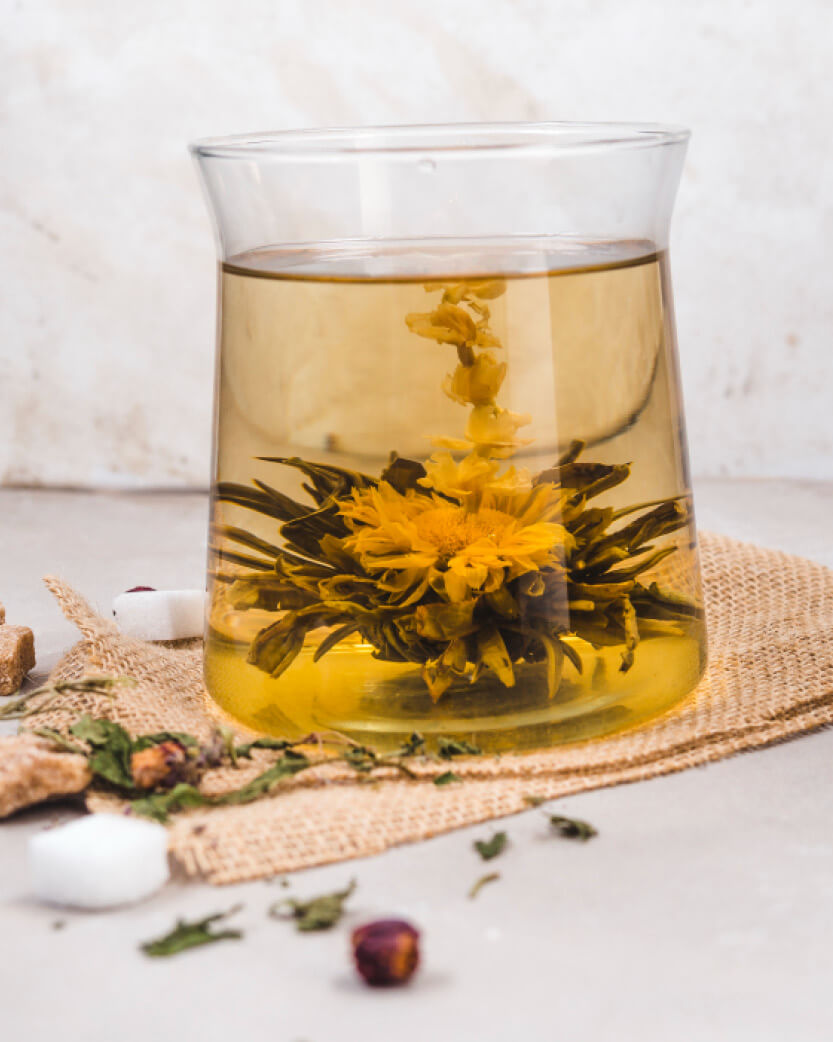 Glass of yellow dandelion floral tea with dried herbs on a textured surface