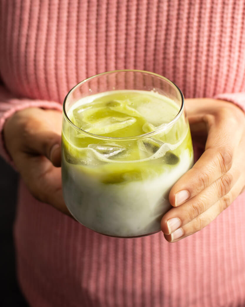 Person holding a glass of iced green and white drink with a pink sweater
