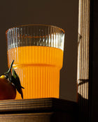 Clear glass filled with orange juice next to a cherry tomato on a wooden surface.