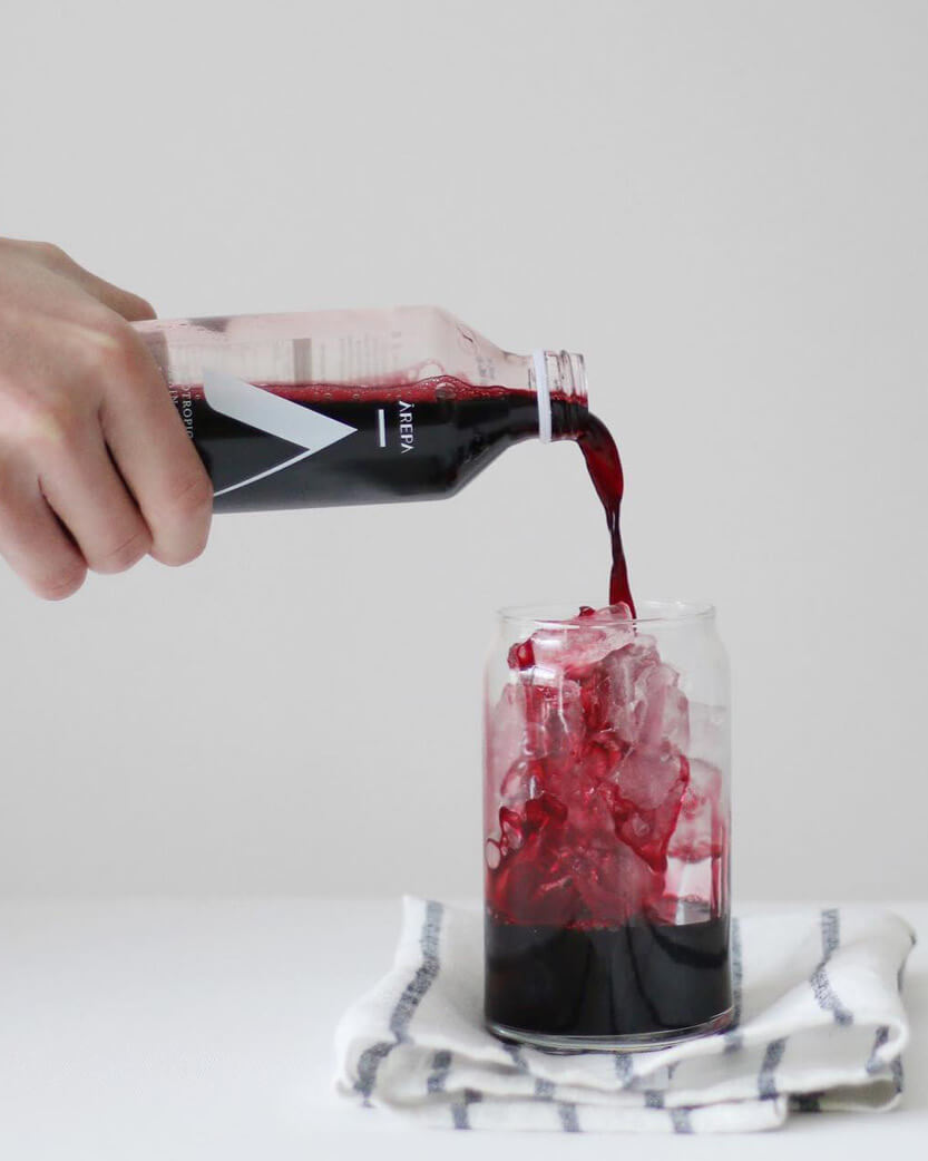 Red liquid being poured from a bottle into a glass with ice on a white background