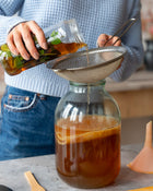 Person pouring liquid into a glass container with a strainer