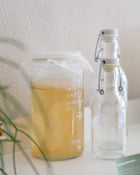 Clear glass bottle with a swing-top lid next to a measuring jug on a light surface.