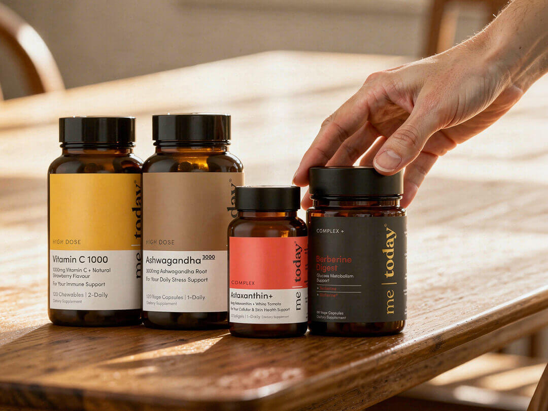 Hand reaching for Me Today supplement bottles on a wooden table.