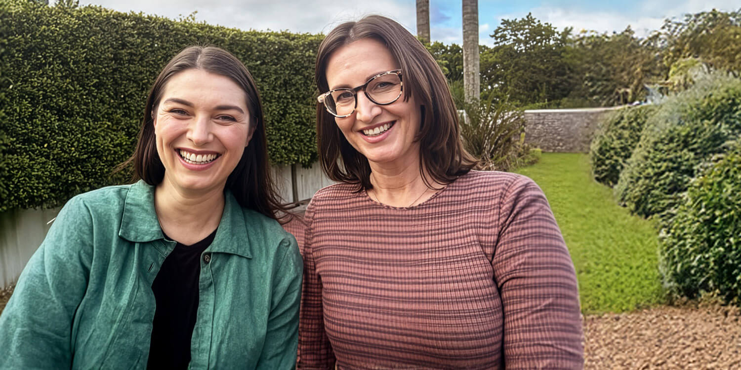 Two women standing outdoors in a garden setting.