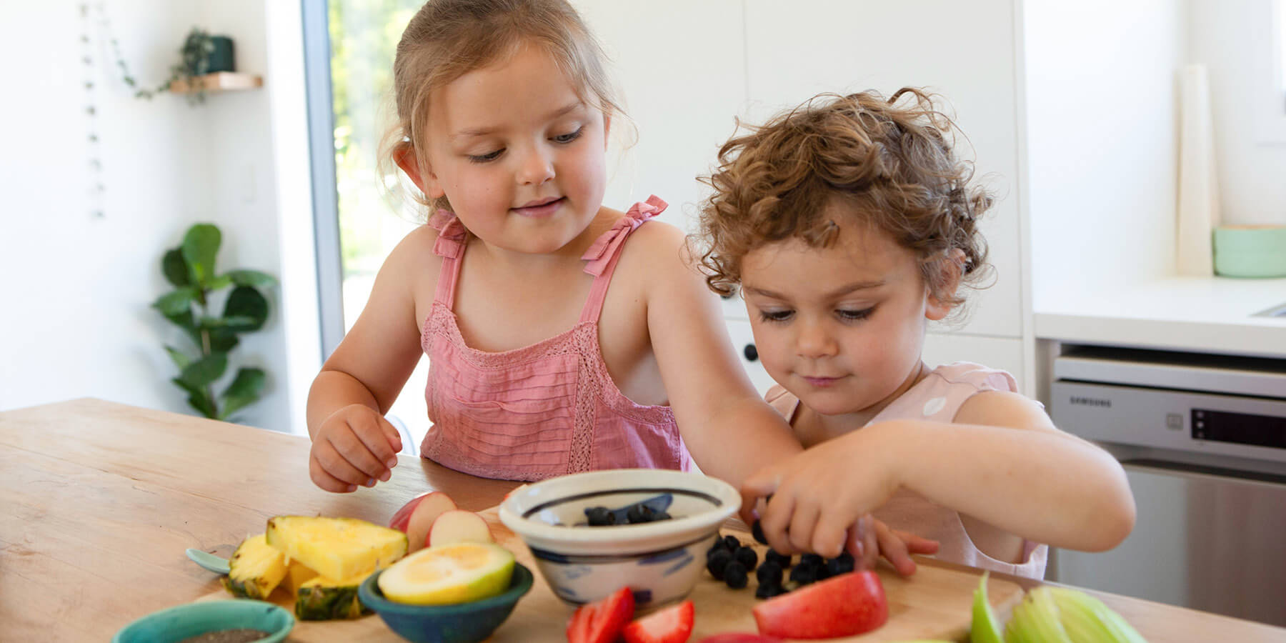 Two girls picking through fruit on a wooden counter.