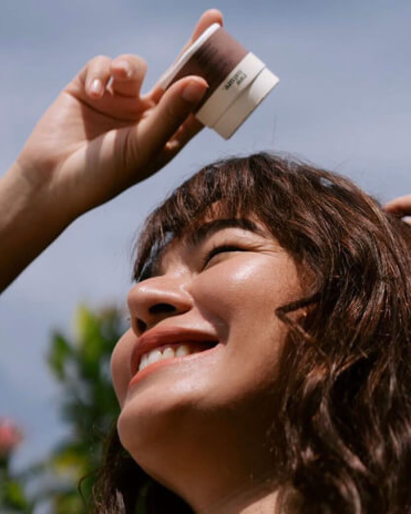 Person applying sunscreen to a woman's face outdoors.