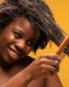 Woman with braided hair using a comb against an orange background.