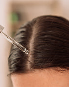 Close-up of a person using a hair dryer on their hair with a blurred background.
