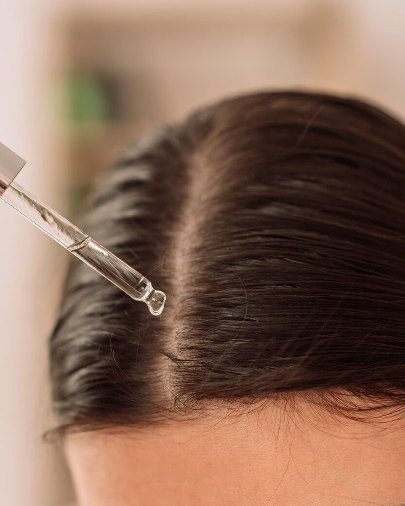 Close-up of a person using a hair dryer on their hair with a blurred background.