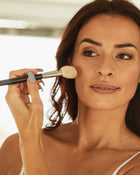 Dark haired woman applying blush with a brush.