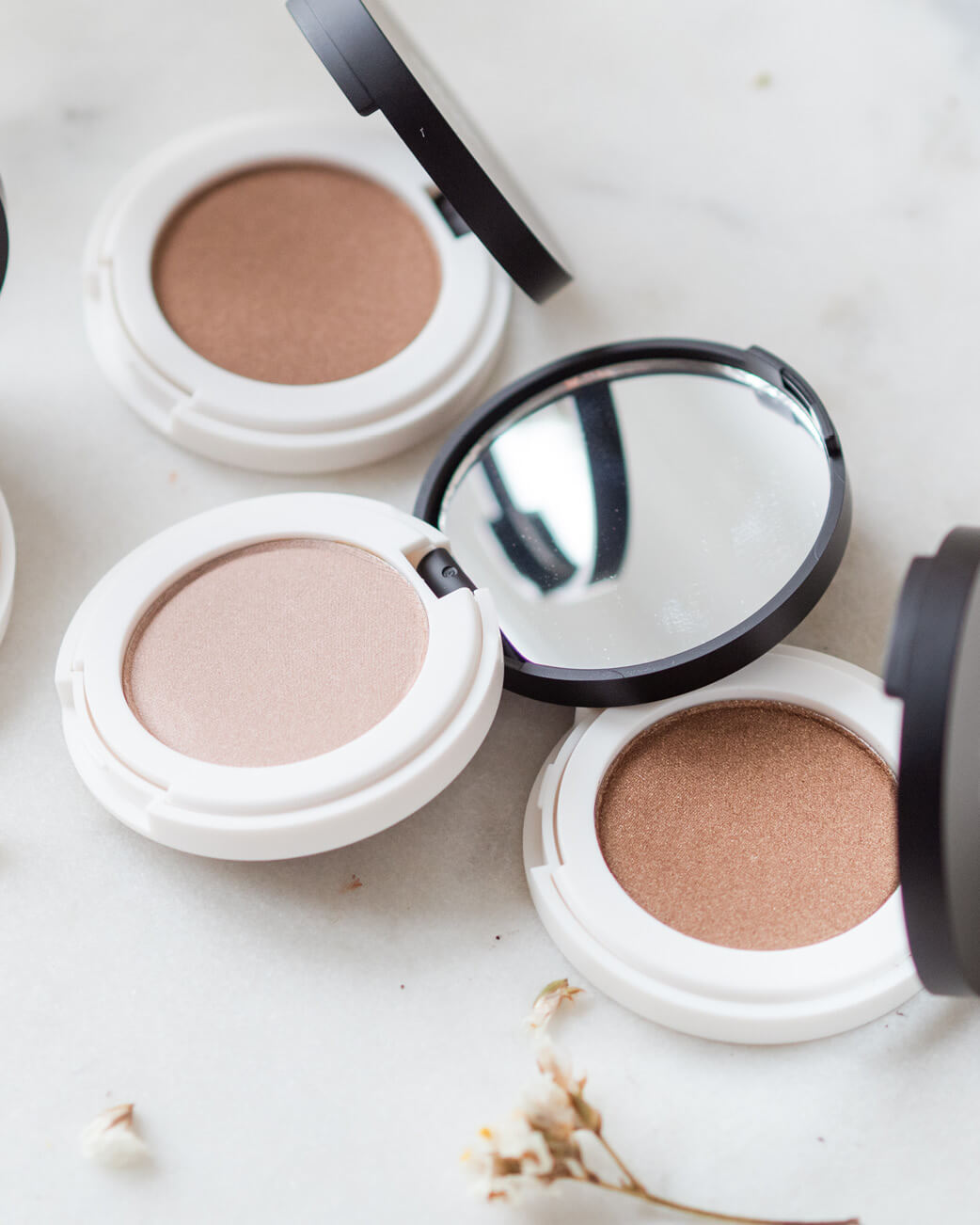 Neutral eyeshadow compacts on a white surface.