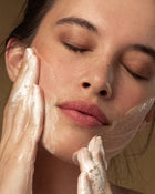 Woman applying a skincare product to her face with a neutral background.