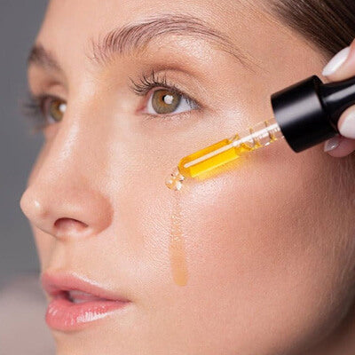 Close-up of a woman's face with a dropper applying a yellow liquid to her skin.