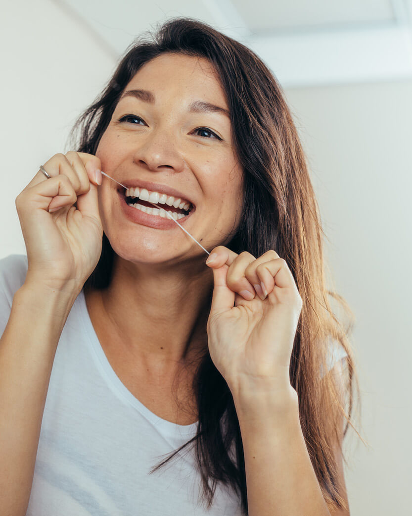 Woman using dental floss with a plain background.
