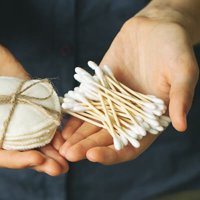 Hands holding a ball of cotton wool and a bundle of cotton buds against a dark background.