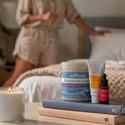 GoodHealth magnesium cream, balm, and dropper on books with a blurred person in the background.