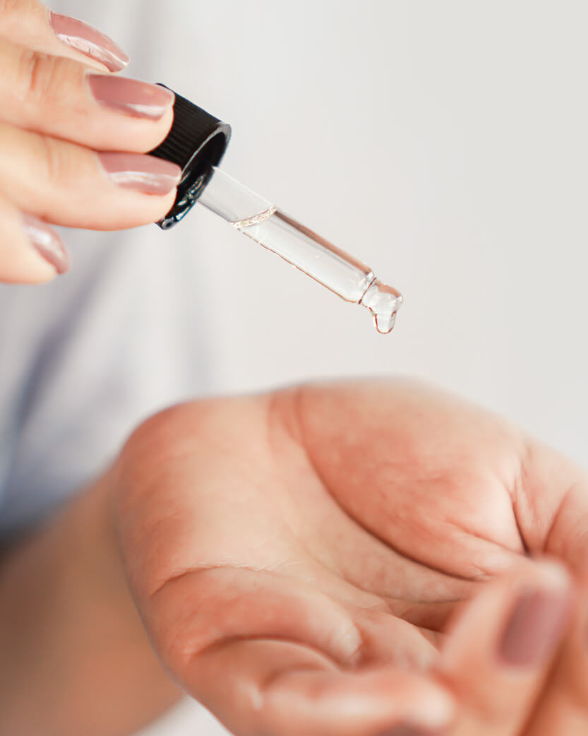 Close-up of a hand holding a dropper with a clear liquid over another hand.