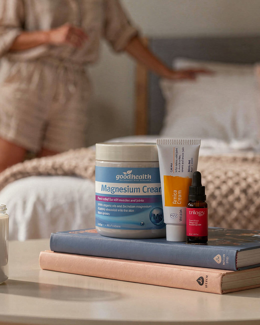GoodHealth magnesium cream, tube, and dropper on books with a blurred person in the background.