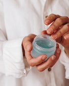 Person holding a small container of blue gel or cream.