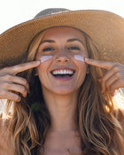 Woman applying sunscreen on her face with a straw hat.