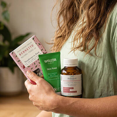 Person holding a bottle of supplements, a box, and a tube of skincare product with visible branding.